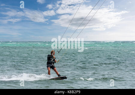 Un homme seul kite surfer rides le long d'une calme vide paradise tropical mer avec fond de l'océan avec ciel bleu et nuages. Banque D'Images