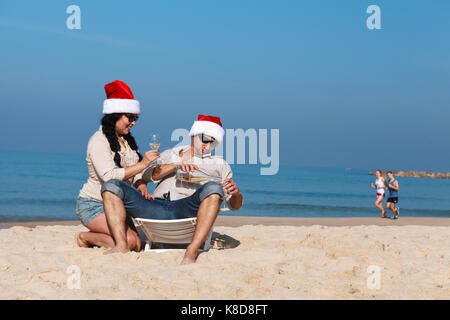 Christmas couple sur une plage de vigne potable autre couple sont en cours d'exécution sur l'arrière-plan Banque D'Images