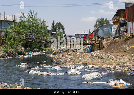 La ligne des baraques taudis rivière Ngong qui est polluée par des déchets, les déchets plastiques et les déchets, un pont en bois de fortune le traverse, Nairobi, Kenya Banque D'Images