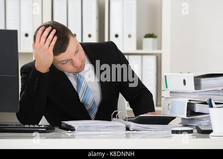 Homme assis comptable tendu avec la tête dans la main at desk in office Banque D'Images