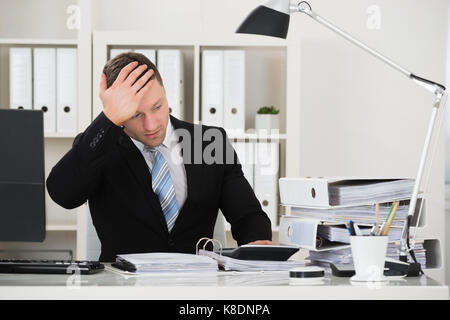 Homme assis comptable tendu avec la tête dans la main at desk in office Banque D'Images