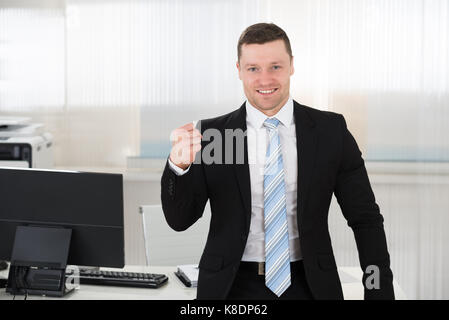 Portrait of businessman clenching fist réussie tout en se tenant à l'ordinateur desk in office Banque D'Images