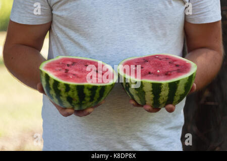 Un jeune homme est titulaire de deux moitiés de melon d'eau dans ses mains. Le concept d'une alimentation saine et le végétarisme. Banque D'Images