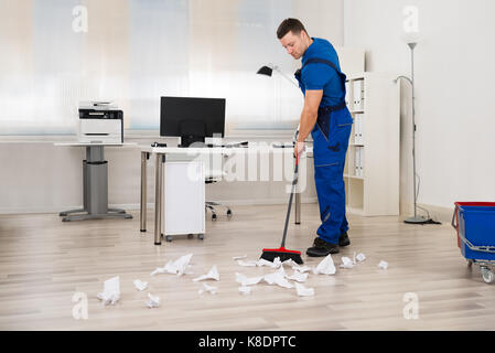 Toute la longueur de l'homme janitor cleaning broom in office Banque D'Images