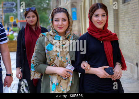 La province du Fars, Shiraz, Iran - 18 avril, 2017 : jeunes femmes iraniennes, vêtus de hijab, sont à pied le long d'une rue de ville avec les smartphones dans leurs mains. Banque D'Images