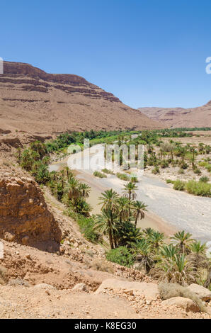 Lit de rivière à sec bordée de palmiers avec orange rouge montagne au Maroc, l'Afrique du Nord. Banque D'Images