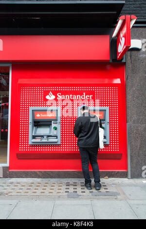 Un jeune homme debout devant un guichet automatique sur Tottenham Court Road, Londres, UK Banque D'Images