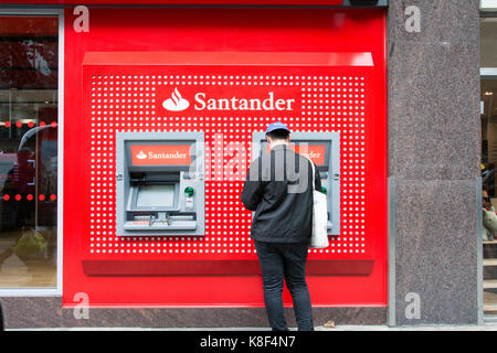 Un jeune homme debout devant un guichet automatique sur Tottenham Court Road, Londres, UK Banque D'Images