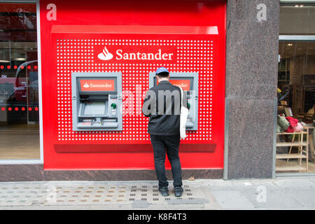 Un jeune homme debout devant un guichet automatique sur Tottenham Court Road, Londres, UK Banque D'Images