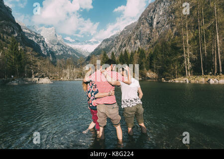 Vue arrière de trois jeunes amis adultes la cheville en lac de montagne, Lombardie, Italie Banque D'Images