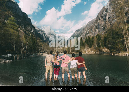 Vue arrière de cinq amis adultes la cheville en lac de montagne, Lombardie, Italie Banque D'Images