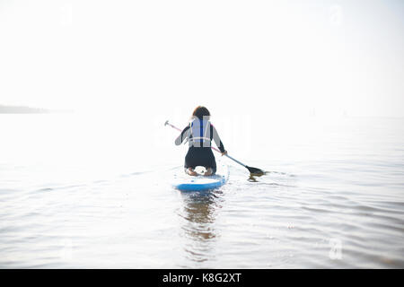 Vue arrière de la pagaie paddleboarder femelle sur la mer brumeuse Banque D'Images