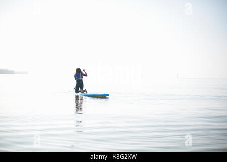 Vue arrière de la pagaie paddleboarder femelle sur la mer brumeuse Banque D'Images