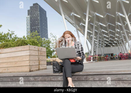 Young businesswoman sitting outside hotel en utilisant un ordinateur portable, New York, USA Banque D'Images