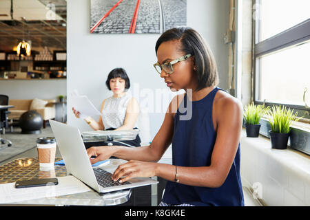 Woman sitting at desk, working on laptop in modern office