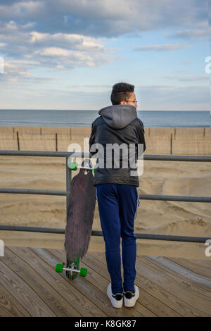 Jeune garçon appuyé contre des garde-corps, à la vue, à skateboard à côté de lui, Asbury, New Jersey, USA Banque D'Images