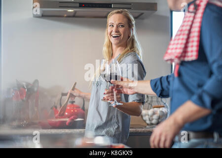 L'homme et de la femme dans la cuisine, la préparation des aliments, tenant un verre de vin, faire un toast Banque D'Images