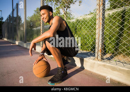 Jeune homme sur un terrain de basket-ball, accroupi avec ball Banque D'Images