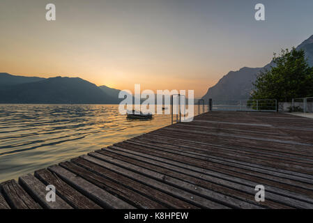 Jetée en bois avec planches en bois et en bateau sur la lac dans le coucher du soleil sur le lac d'Iseo et les montagnes environnantes, lombary, italie Banque D'Images