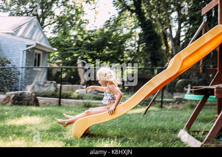 Playful girl jouant sur la diapositive à l'aire de jeux Banque D'Images