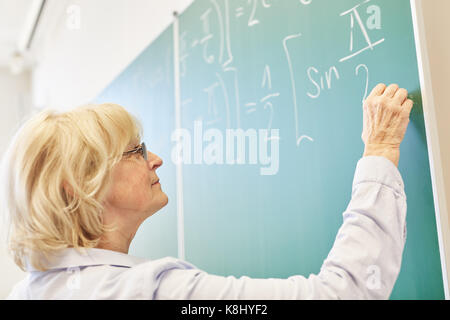 Senior woman comme enseignant à l'université de mathématiques écrit on chalkboard Banque D'Images