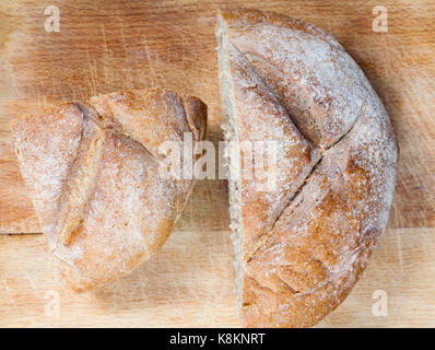 Couper en deux moitiés d'une ronde de pain fraîchement cuit au four, couleur de lumière à partir de la farine de blé. photo gros plan, vue d'en haut. la cuisson se trouve sur une table en bois Banque D'Images
