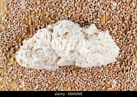 Une partie de la pâte de blé une miche de pain avec une croûte déchirés, couché avec les grains entiers de blé. photo gros plan, Vue de dessus Banque D'Images