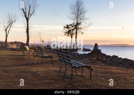 Assis sur des bancs d'un lac au coucher du soleil Banque D'Images