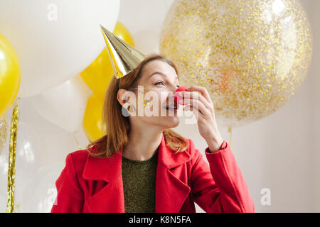 Jeune femme dans un chapeau de fête de jouer à une partie sur le contexte de baisse confetti Banque D'Images