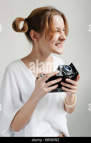 Close up portrait of a smiling pretty girl taking photo sur un appareil photo rétro isolated over white background. Banque D'Images