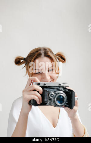 Close up portrait of a smiling pretty girl taking photo sur un appareil photo rétro isolated over white background. Banque D'Images