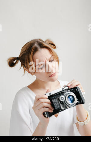 Close up portrait of a smiling pretty girl taking photo sur un appareil photo rétro isolated over white background. Banque D'Images