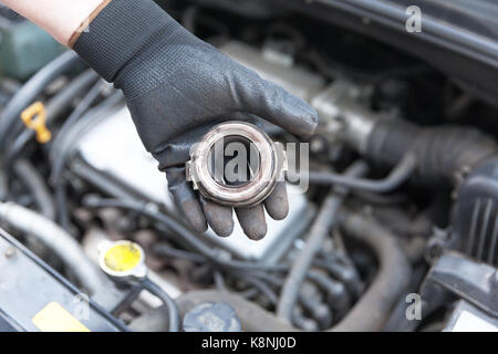 Mécanicien auto portant des gants de travail holding old la butée d'embrayage sur le moteur d'un véhicule Banque D'Images