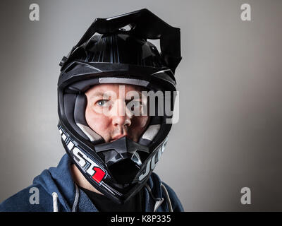 Un homme portant un bike rider motocross casque intégral noir debout contre un arrière-plan clair. Banque D'Images