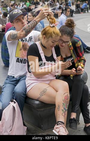 Un jeune homme les cheveux de sa petite amie liens en tresses alors qu'elle et un ami vérifier quelque chose sur son téléphone cellulaire. À Greenwich Village, New York City Banque D'Images