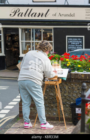 Artiste féminine en peinture d'un magasin local à l'aide de peinture et un chevalet à Arundel, West Sussex, Angleterre, Royaume-Uni. Banque D'Images