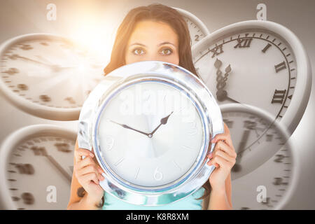 Belle brune tenant un réveil contre ordinateur image d'horloges de mur Banque D'Images