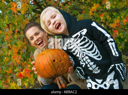 Trick or Treat. smiling modern la mère et l'enfant au parc montrant halloween citrouille sculptée Banque D'Images