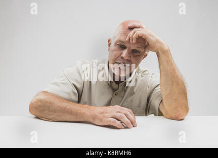 Découragé senior man sitting penser avec sa tête sur sa main les yeux fixés sur la table avec une expression grave Banque D'Images