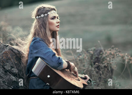 Belle fille hippie avec guitare assis sur l'herbe près de stone Banque D'Images