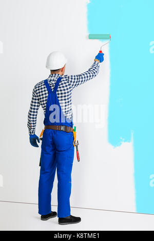 Portrait de la vue arrière du peintre man painting the wall in blue with copy space Banque D'Images