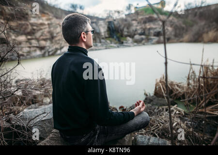 Man meditating in lotus pose sur une falaise rocheuse avec vue sur la rivière. concept zen Banque D'Images