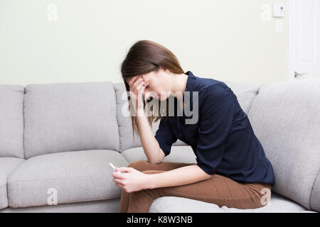 Fille assise sur un canapé à la maison lors de la lecture des résultats de son test de grossesse récente Banque D'Images