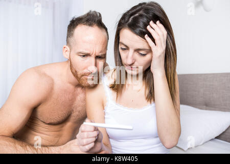 Cheerful couple trouver les résultats d'un test de grossesse sitting on bed Banque D'Images