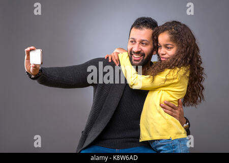 Un père noir prenant selfie avec un smartphone alors que sa jeune fille l'embrasse Banque D'Images