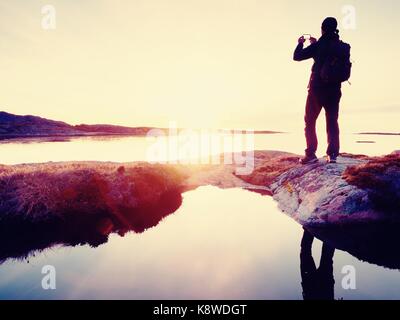 Silhouette arrière de voyager en prenant l'homme en mer. selfies touriste avec sac à dos, debout sur un rocher, à plus de bleu de la mer et prendre photo de son smart Banque D'Images