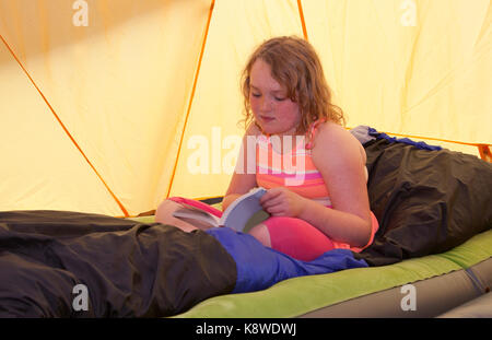 Fille aux cheveux rouges de rousseur lit un livre à l'intérieur d'une tente en camping Banque D'Images