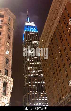 Une photo qui donne sur l'Empire State Building la nuit depuis le niveau de la rue. La partie supérieure est éclairée par des lumières bleues et protégée dans un nuage bas. Banque D'Images