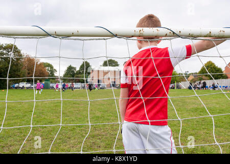 Un jeune garçon portant un arsenal kit, dans l'objectif permanent au cours d'un match de football joué par de jeunes garçons Banque D'Images