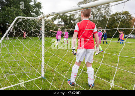 Un jeune garçon portant un arsenal kit, dans l'objectif permanent au cours d'un match de football joué par de jeunes garçons Banque D'Images